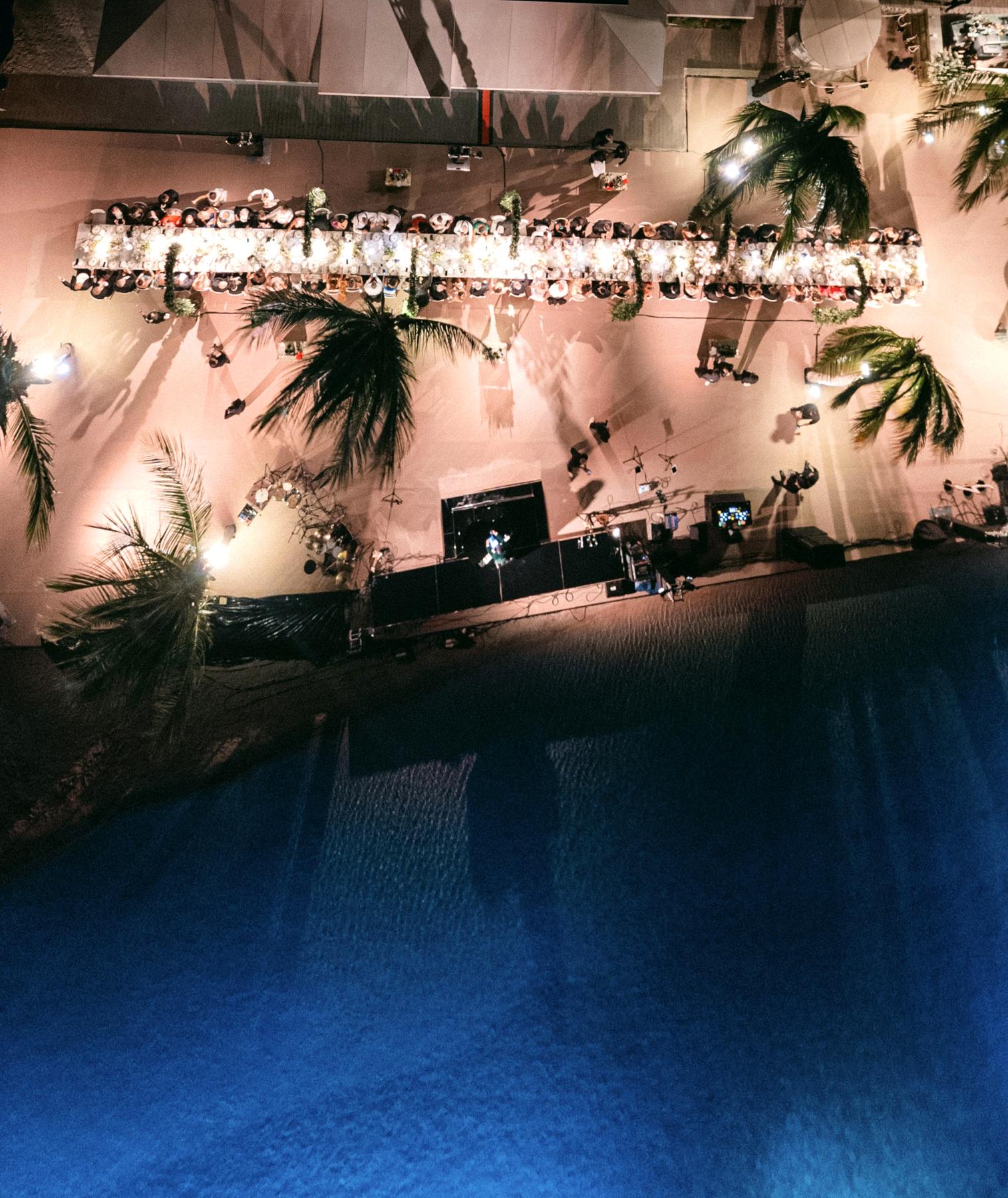 Luchtfoto bij nacht van een stranddiner aan lange tafel bij zee met stralende kroonluchters, Curacao